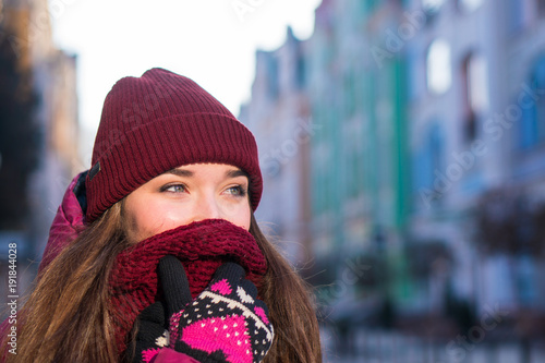 Pretty Brunette Girl Wearing Purple Winter Coat, Hat and Scarf, Walking by European Street at Winter, Wrapped up in a Scarf. © Oleksandr