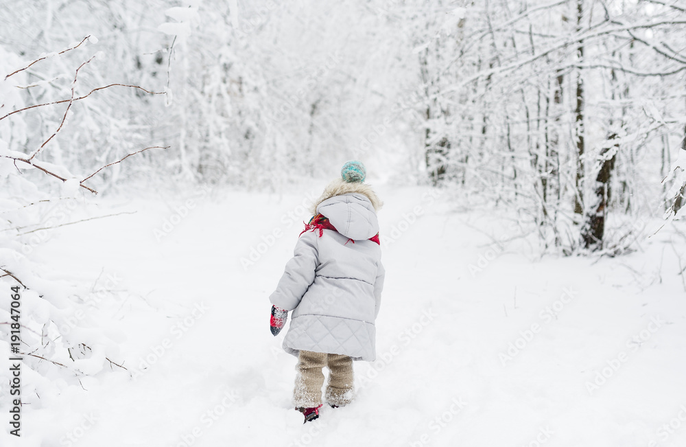Back view of a little girl in a snowsuit walking through a snowy path with deep snow banks on either side. Back view of a little girl in a snowsuit walking through a snowy path with deep snow banks on either side.