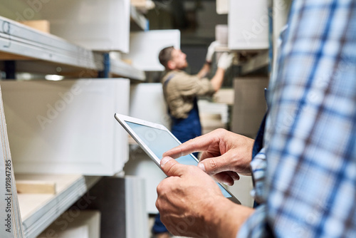 Close up view of unrecognizable worker holding digital tablet while doing inventory in factory storage room, copy space