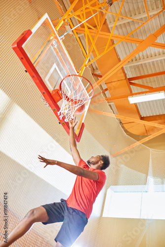 Below view of strong determined young African-American basketball player slam dunking jumping in air, training before game © Seventyfour
