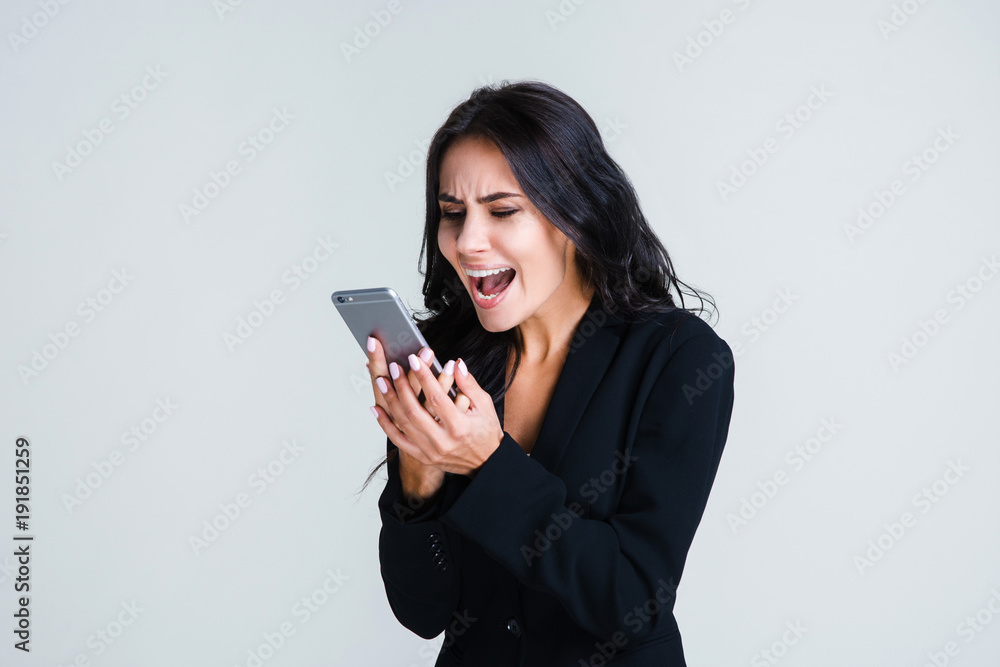 Do you hear me? Beautiful young businesswoman using her smartphone and looking irritated while standing against white background Do you hear me? Beautiful young businesswoman using her smartphone and looking irritated while standing against white background