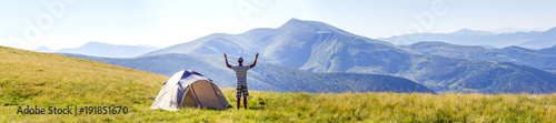 Hiker meets good morning with raised hands just got out from tent in mountains.