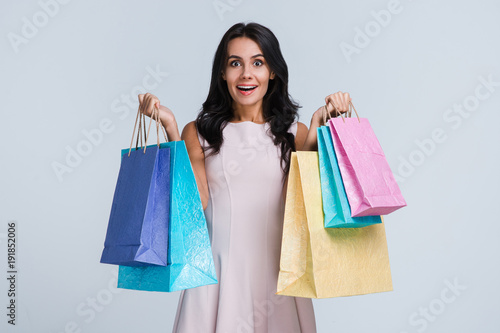 Perfect shopping. Beautiful young woman holding shopping bags and looking at camera with smile while standing against white background