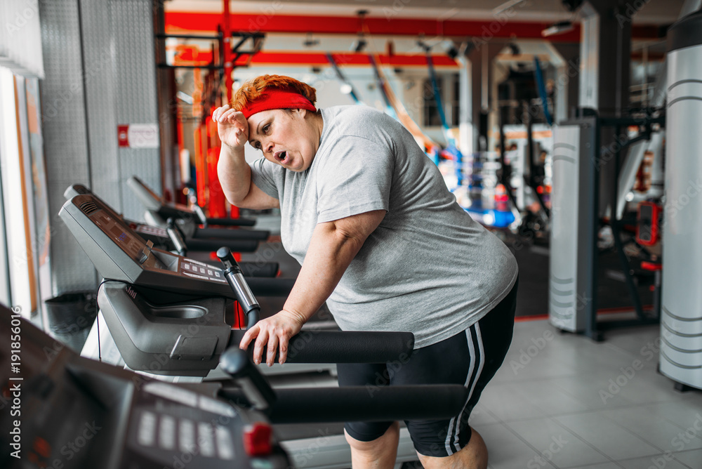 Overweight woman running on a treadmill in gym