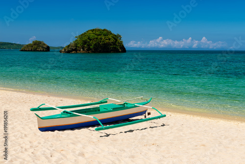 fishboat on sand and two small islands on tropic turquoise sea and blue sky.
