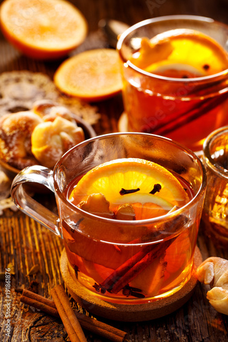 Spicy citrus hot tea with ginger, cloves, cinnamon and orange slices, delicious, warming and healthy in glass cups on a wooden table