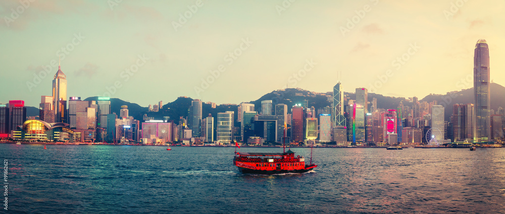 Obraz premium Spectacular skyline of Hong Kong island, China, with skyscrapers and historic boat sailing at sunset. Panoramic travel background.