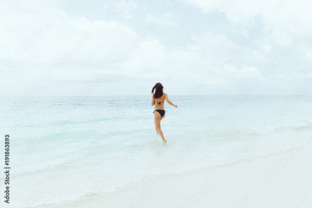 Summer background. Young woman runs into ocean
