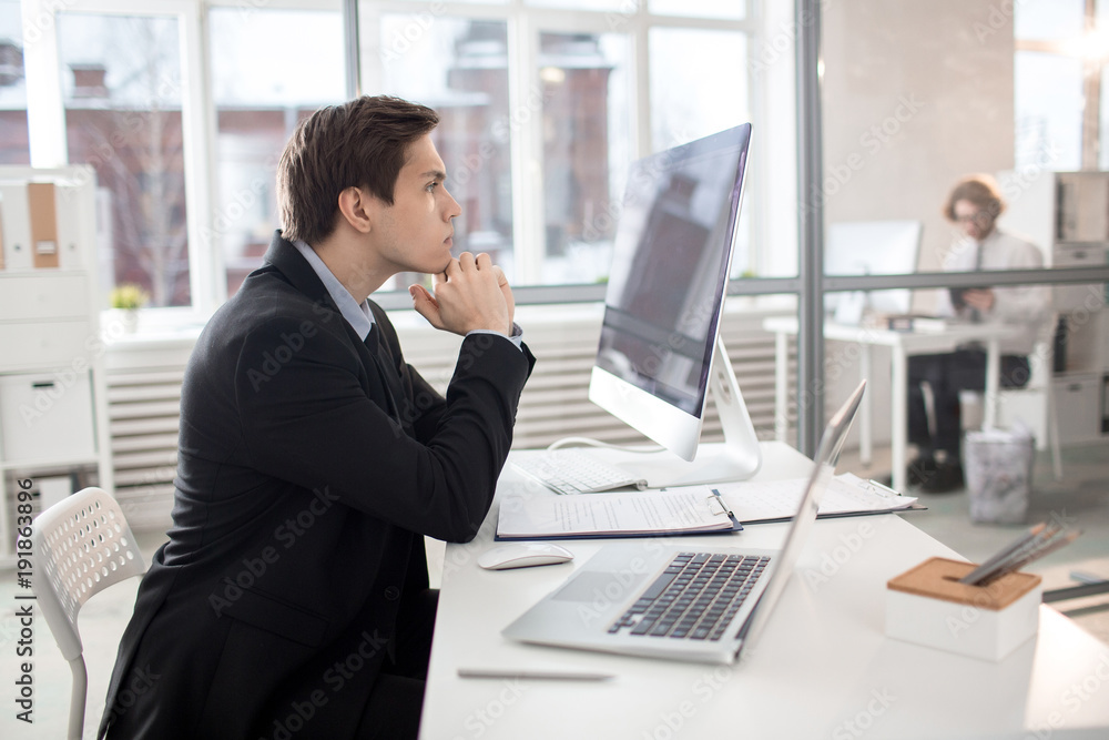Serious young businessman sitting by his desk and concentrating on financial analysis Serious young businessman sitting by his desk and concentrating on financial analysis