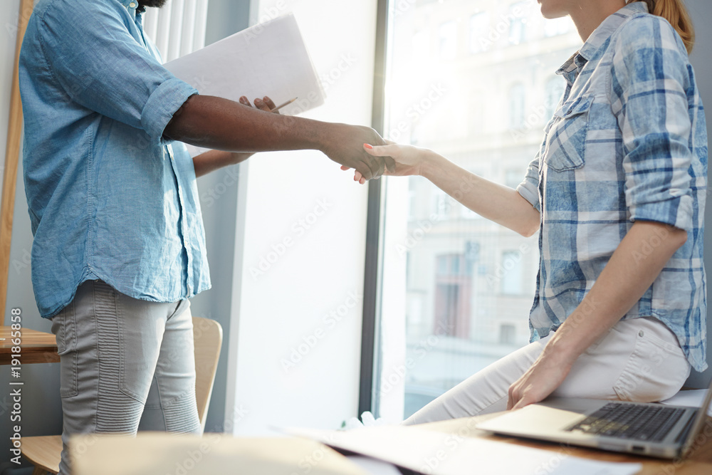 Intercultural business partners handshaking after signing new contract in office Intercultural business partners handshaking after signing new contract in office