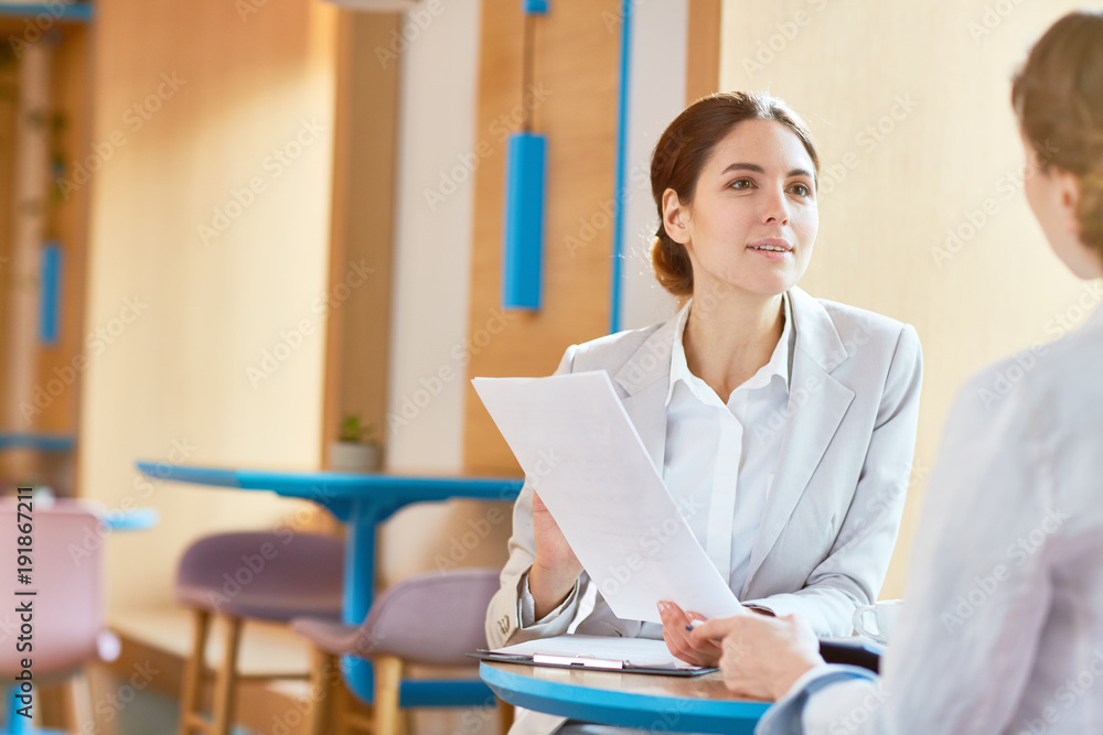 Young female agent with business document talking to one of clients during appointment in cafe Young female agent with business document talking to one of clients during appointment in cafe