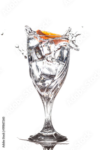 Orange slice splashing into glass of water with ice cubes