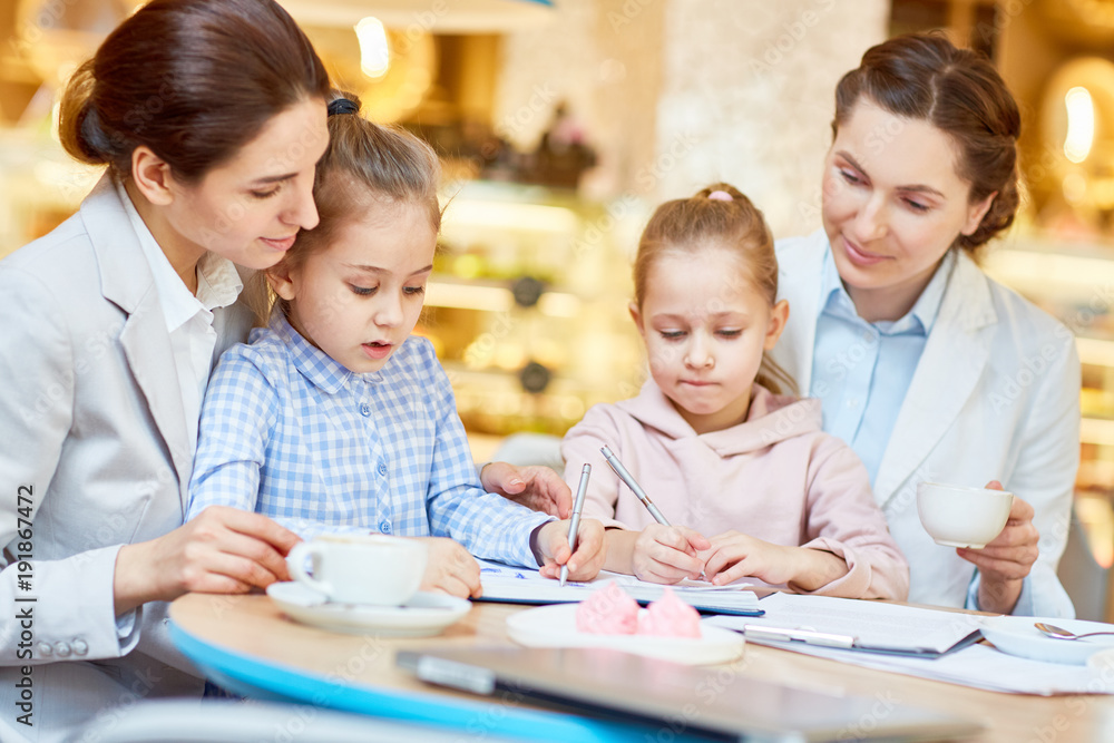 Young businesswomen looking what their daughters drawing while spending time together in cafe Young businesswomen looking what their daughters drawing while spending time together in cafe
