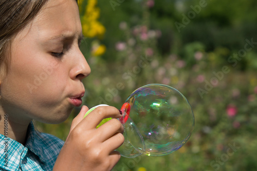 A girl in a plaid shirt is playing with soap bubbles