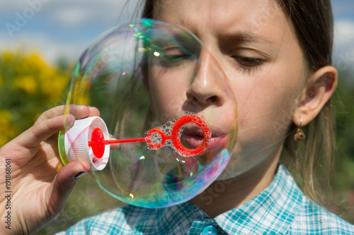 A girl in a plaid shirt is playing with soap bubbles