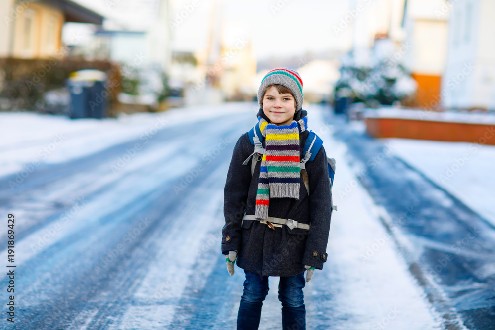 Happy kid boy with backpack or satchel having fun with snow on way to school Happy kid boy with backpack or satchel having fun with snow on way to school