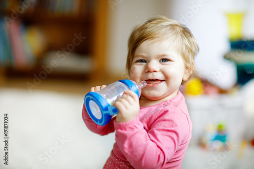 Cute adorable ewborn baby girl holding nursing bottle and drinking formula milk or water photo