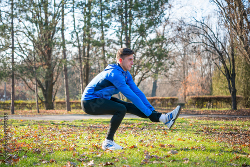 Young Male Runner Stretching in the Park in Cold Sunny Autumn Morning. Healthy Lifestyle and Sport Concept.