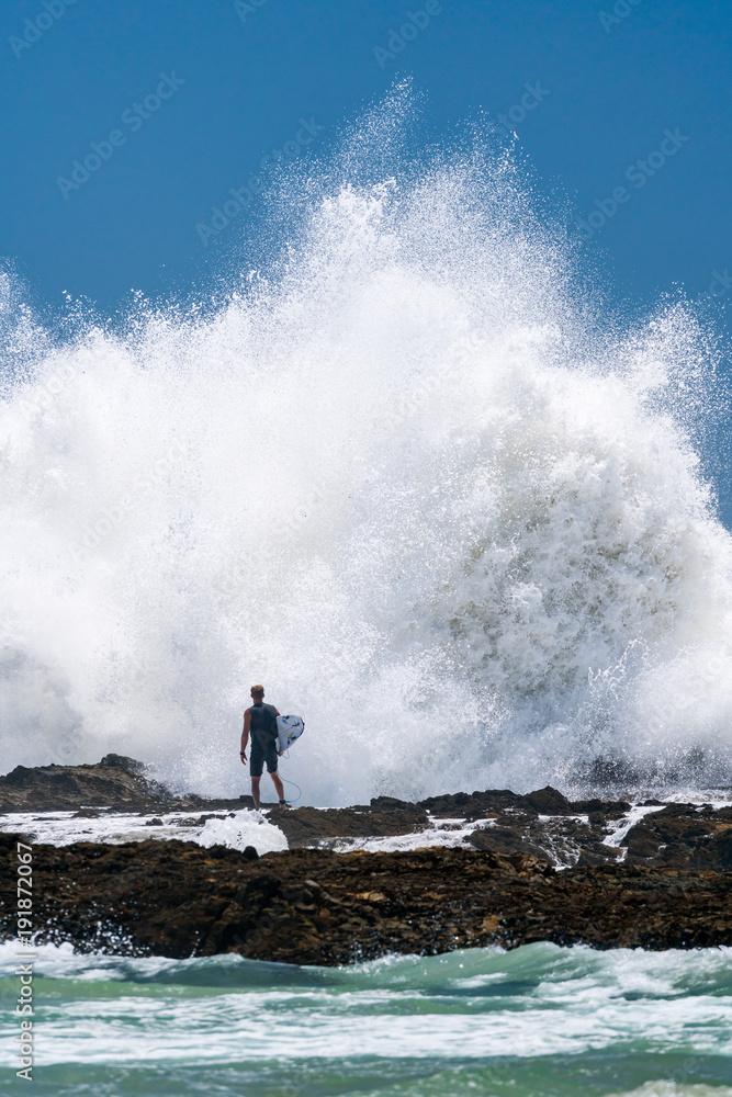 Obraz premium A surfers stands at the shore at Snapper Rocks on the Gold Coast, Queensland, as a wave crashes in front of him.