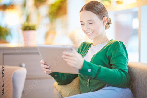 Smiling girl with tablet watching webcast while relaxing at leisure
