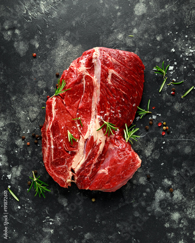 Fresh Raw braising steak on black background with rosemary, pepper, salt