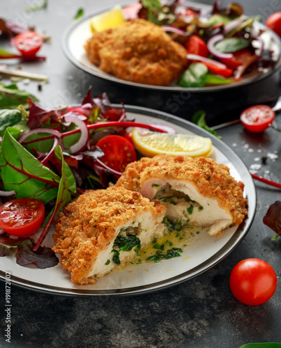 Breaded Chicken Kiev breast stuffed with butter, garlic and herbs served with vegetables in a plate.