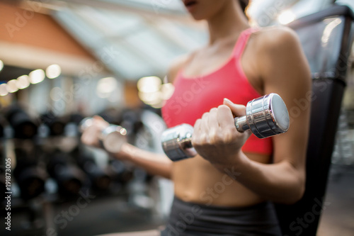 Midsection of sporty girl with dumbbells exercising in fitness club