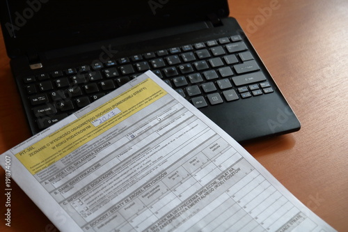Formularz podatkowy, polski, leży na czarnym otwartym laptopie, na brązowym biurku