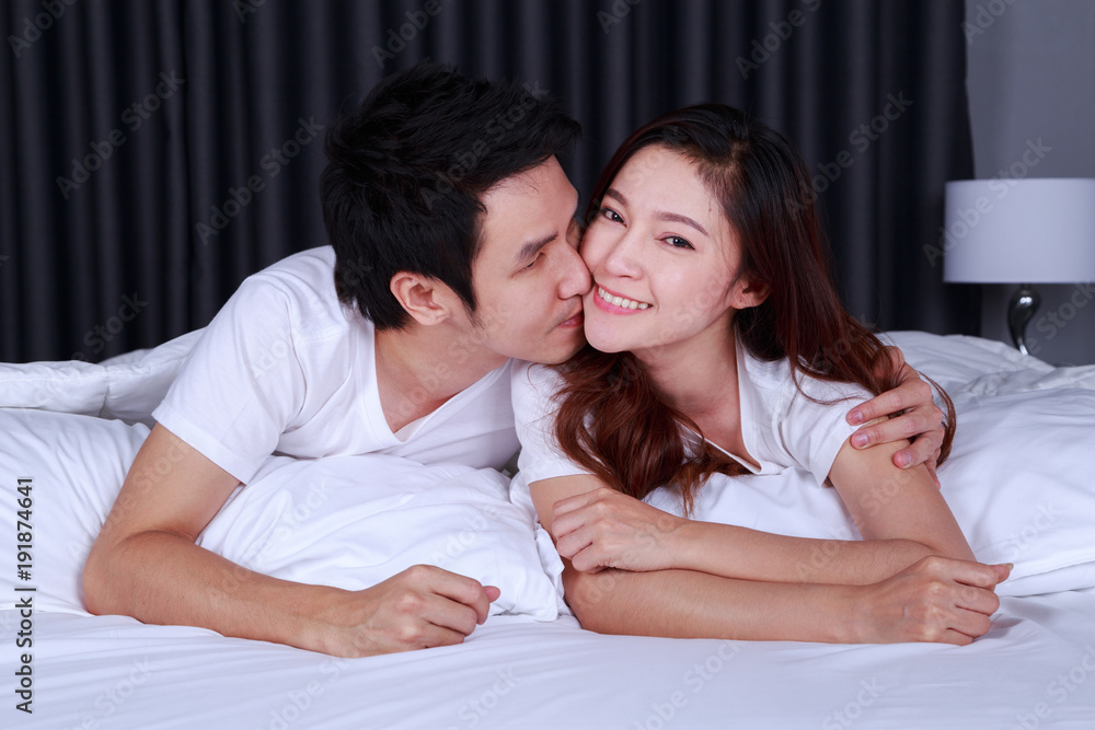 man is kissing his beautiful smiling wife in cheek on bed man is kissing his beautiful smiling wife in cheek on bed