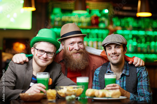 Three happy and friendly men in hats having beer in pub on Saint Patrick day