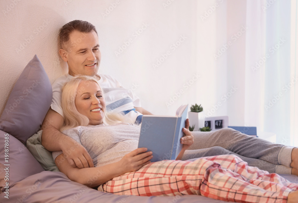 Senior couple reading book on bed together Senior couple reading book on bed together