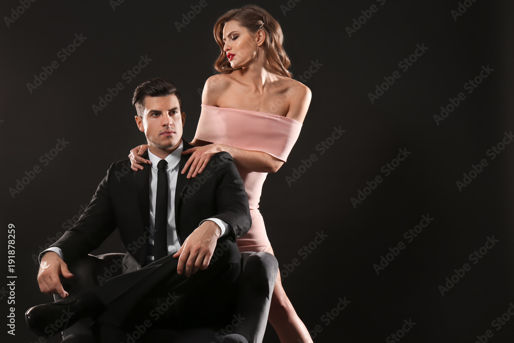 Businessman wearing suit sitting in armchair and sexy woman on dark background Businessman wearing suit sitting in armchair and sexy woman on dark background