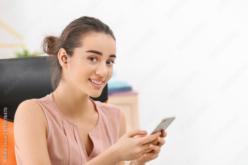 Young woman with hearing aid using smartphone indoors Young woman with hearing aid using smartphone indoors