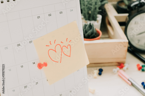 post note paper with couple heart sticky on calendar and business equipment clock, plant background. image for copy space, business, office, celebration concept