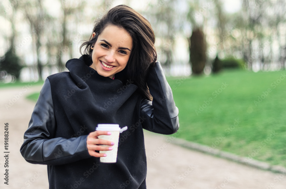 a beautiful girl in a black coat , walks in the Park and drinking coffee a beautiful girl in a black coat , walks in the Park and drinking coffee
