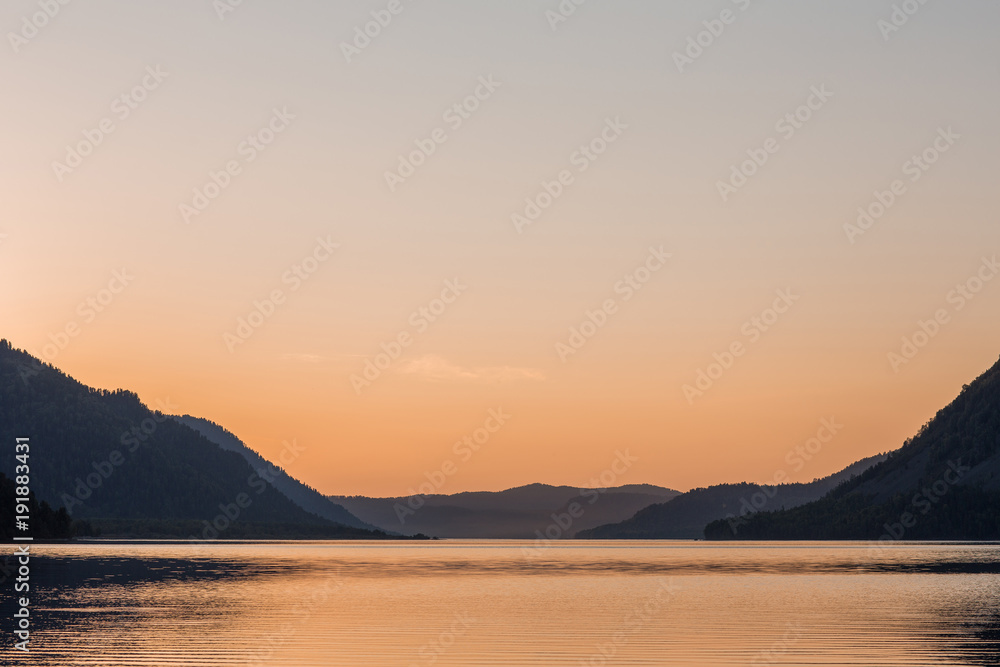 Beautiful mirror surface of a mountain lake at sunset with a warm and level sky