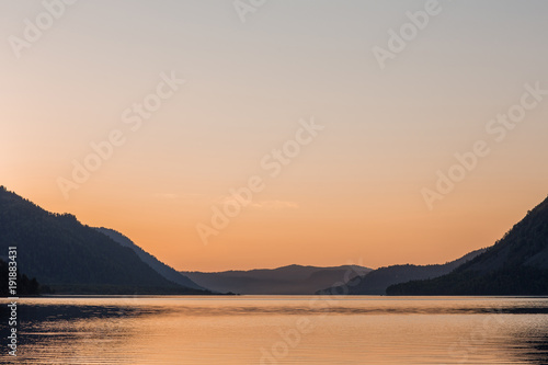Beautiful mirror surface of a mountain lake at sunset with a warm and level sky © ivan_kuznetsov