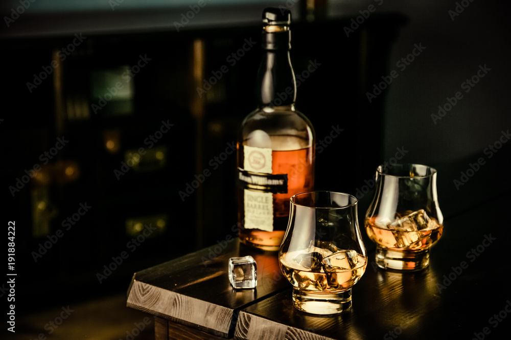 Whiskey in glasses with ice on rustic background