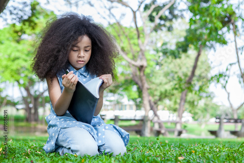 little gir sitting on grass and reading a book in the park