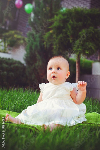 half-year-old child sitting on the grass in the yard, dressed in a white dress rejoices, 6 months. Concept education of children, children's goods © lanarusfoto