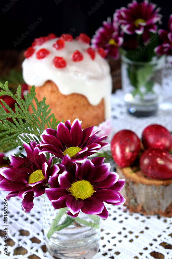 Three spring flowers. Easter cake and red coloured eggs in the background. Easter composition Three spring flowers. Easter cake and red coloured eggs in the background. Easter composition