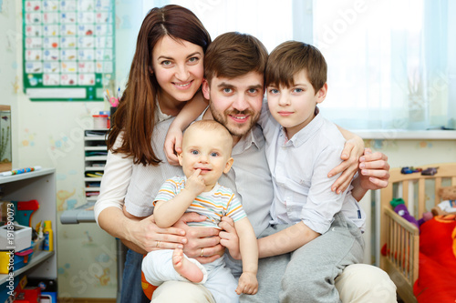 A young family with two children boys sitting on lap looking at camera and smiling. Happy family concept.