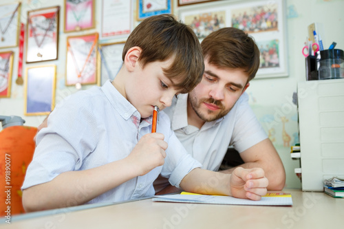 Little boy doing home work in his room with tutor. Adult man helping child concept photo