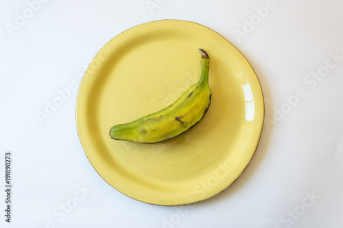 Half ripe Burro banana on bright yellow plate, also Orinoco, Bluggoe, Horse, Hog or Largo banana, isolated on white, horizontal aspect photo