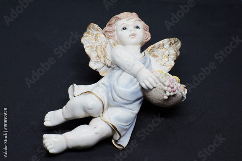 Isolated little angel with basket of fruits and blue tunic looking at the sky on black background. Closeup