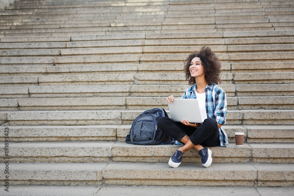 Smiling student sitting on stairs using laptop Smiling student sitting on stairs using laptop