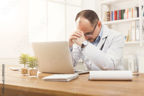 Portrait of tired doctor in glasses sitting at the desktop