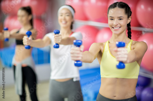 Group of young women with dumbbells working out in fitness center