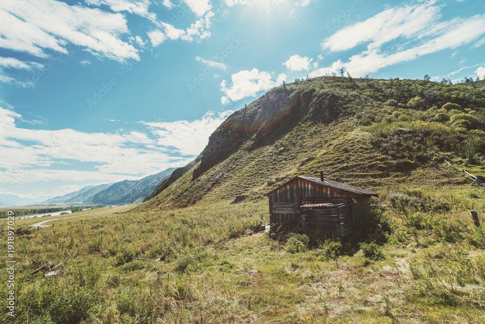 Solitary forsaken hovel on the flank of hill surround by pastures of native grasses; with mountain ridge stretching into hazy distance, river, and dirt road; Kuyus district, Altai, Russia