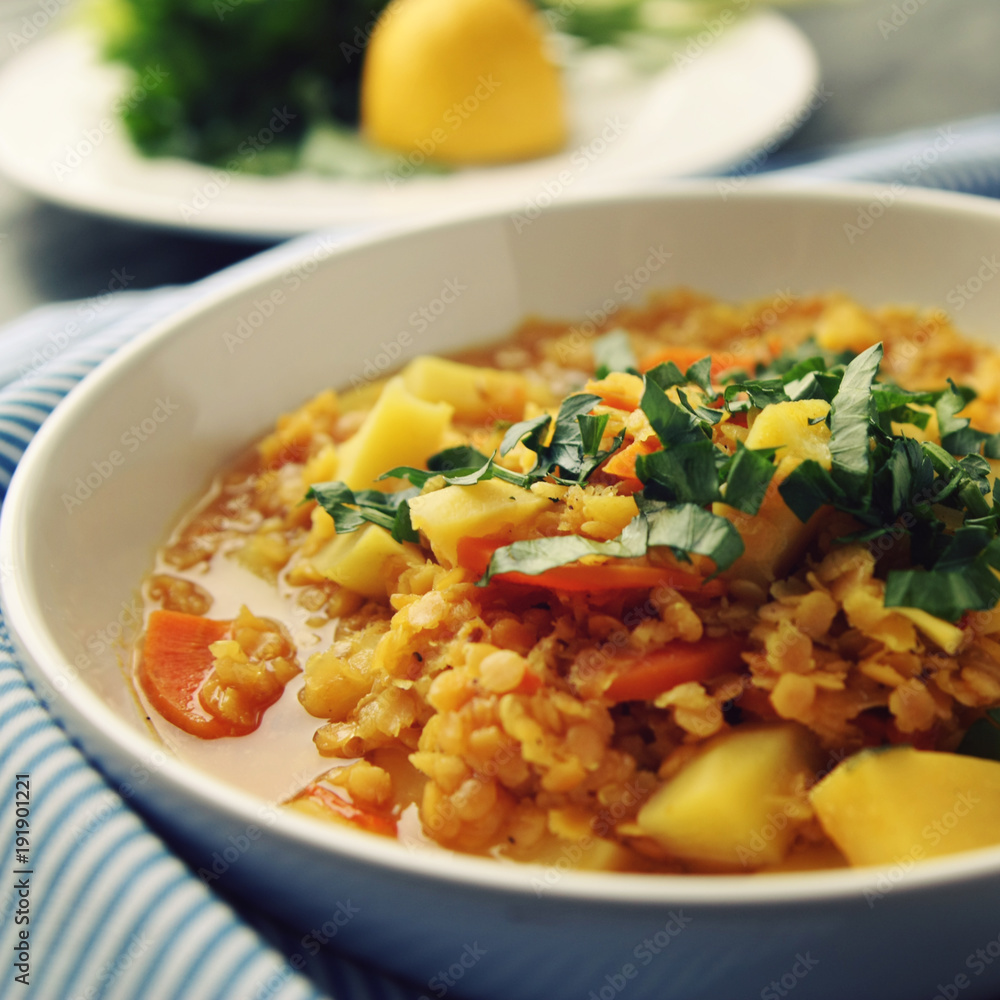 Red lentil stew on the round white plate. Vegetarian dish with potato, carrot and turmeric. European cuisine. Colorful vegan lunch. Selective focus. Red lentil stew on the round white plate. Vegetarian dish with potato, carrot and turmeric. European cuisine. Colorful vegan lunch. Selective focus.